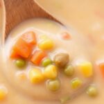 A bowl of creamy Stampede Soup garnished with fresh herbs, served with a side of crusty bread.